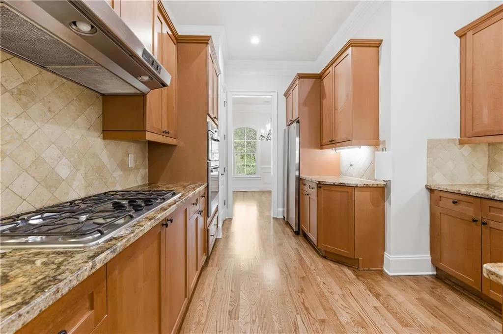 Kitchen featuring decorative backsplash, ornamental molding, stainless steel appliances, light wood-style flooring, and light stone countertops