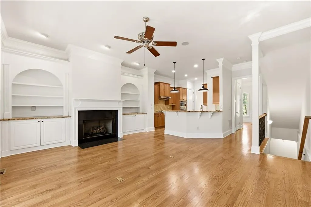 Unfurnished living room with built in shelves, a fireplace with flush hearth, a ceiling fan, light wood-style flooring, and ornamental molding