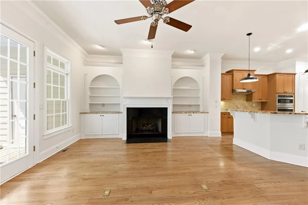 Unfurnished living room with crown molding, ceiling fan, light wood finished floors, a fireplace with flush hearth, and built in features