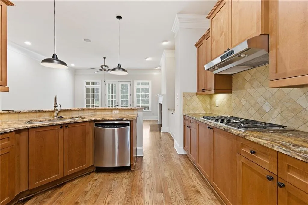 Kitchen with light wood-style flooring, stainless steel appliances, light stone countertops, crown molding, and decorative light fixtures