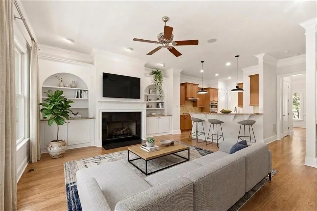 Living room with ceiling fan, built in features, a fireplace with flush hearth, ornamental molding, and light wood-style floors