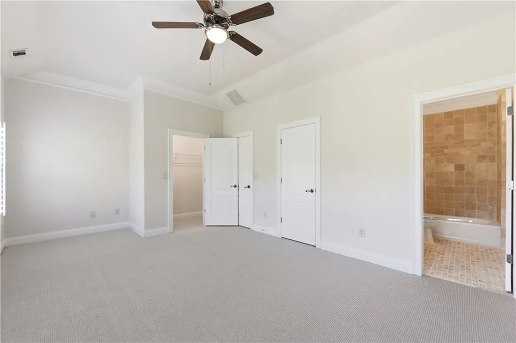 Unfurnished bedroom featuring light colored carpet, a walk in closet, ceiling fan, lofted ceiling, and connected bathroom