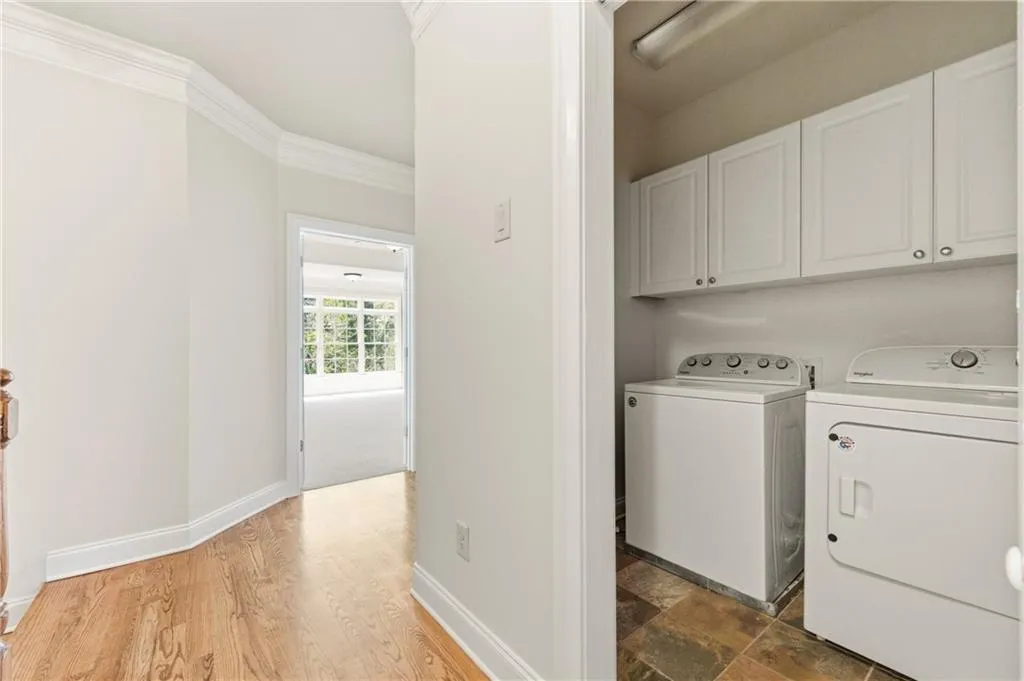 Laundry area with cabinet space, ornamental molding, washing machine and clothes dryer, and light wood-type flooring