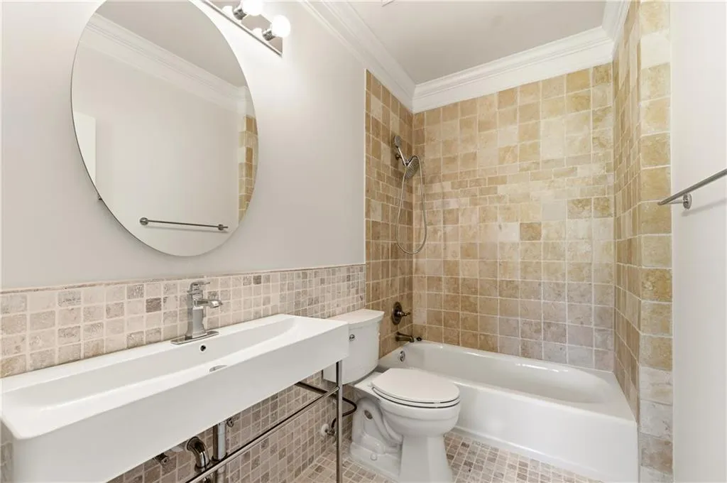 Full bathroom featuring tile walls, crown molding, washtub / shower combination, and wainscoting