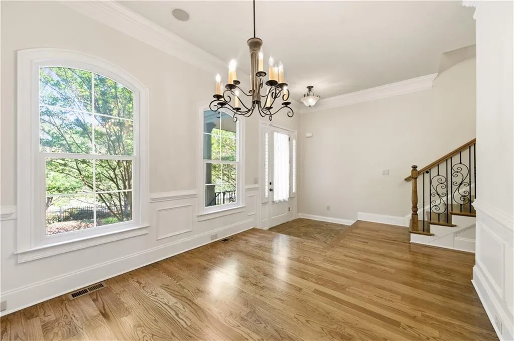 Foyer featuring a decorative wall, crown molding, a wainscoted wall, light wood finished floors, and hanging lights