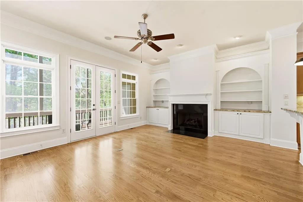 Unfurnished living room with built in shelves, ornamental molding, french doors, ceiling fan, and light wood-type flooring