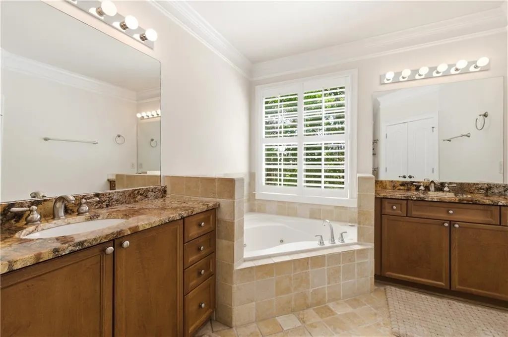 Bathroom featuring ornamental molding, two vanities, a jetted tub, and light tile patterned flooring