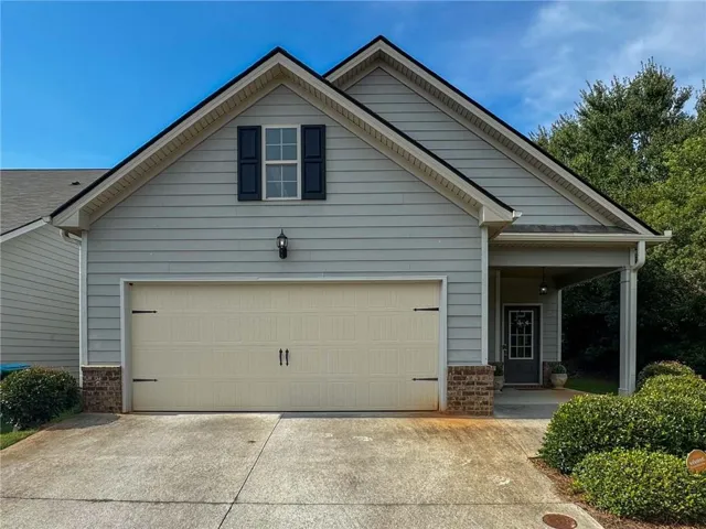 Exterior featuring light-colored siding with dark shutters, an attached garage with decorative hardware, a covered porch entry, and established perimeter landscaping