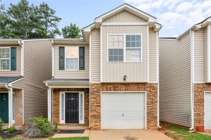 Two-story townhouse exterior with a stone facade accent, vertical and horizontal siding, a single-car garage, and a black paneled entry door with sidelights