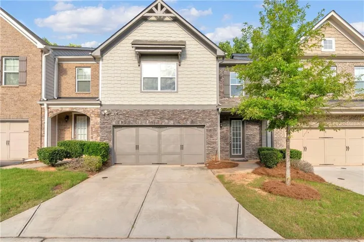 Multi-level townhome exterior featuring an attached two-car garage, stone and shake siding accents, a prominent gable, and a concrete driveway