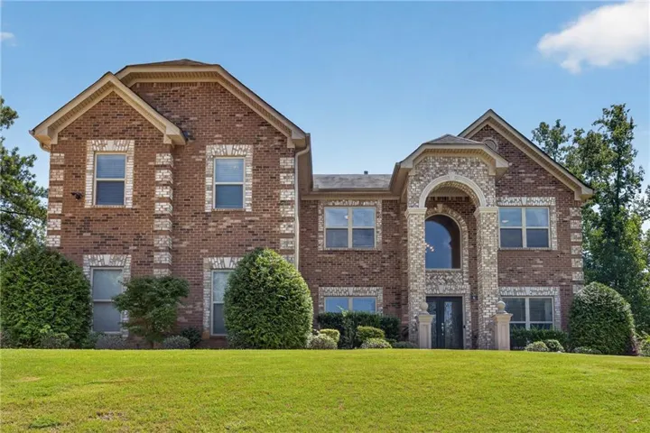 Brick exterior with decorative stone accents, arched entry, multiple windows, and a manicured lawn