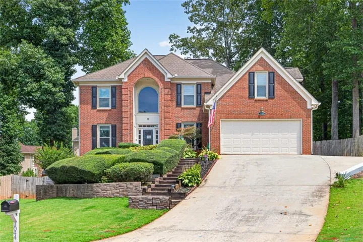 Brick exterior featuring a two-car garage and added parking pad