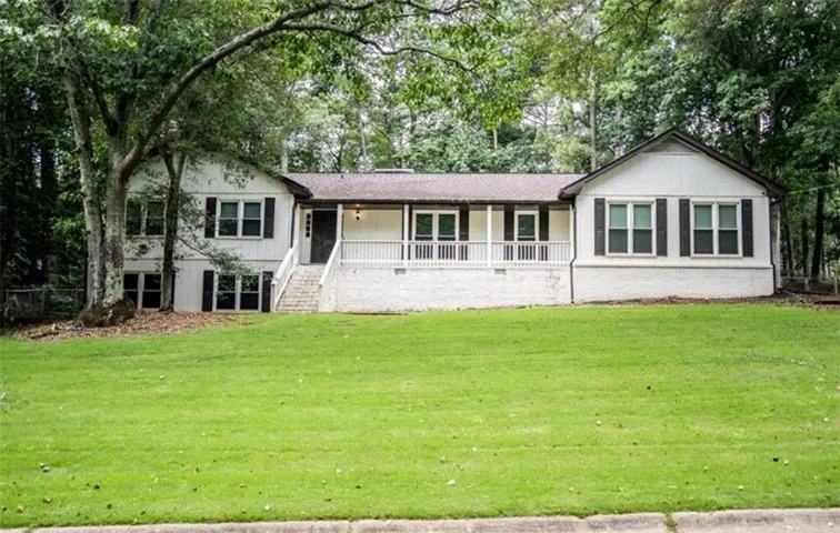 White exterior with dark shutters, covered front porch, white porch railing, and a gabled roofline