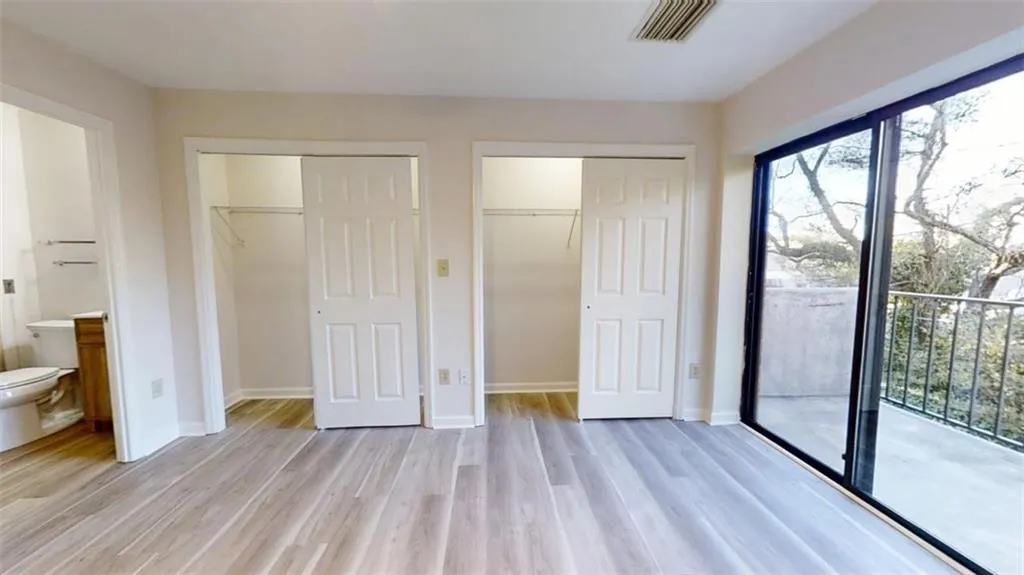 Unfurnished bedroom with light wood-style floors, multiple windows, connected bathroom, and baseboards