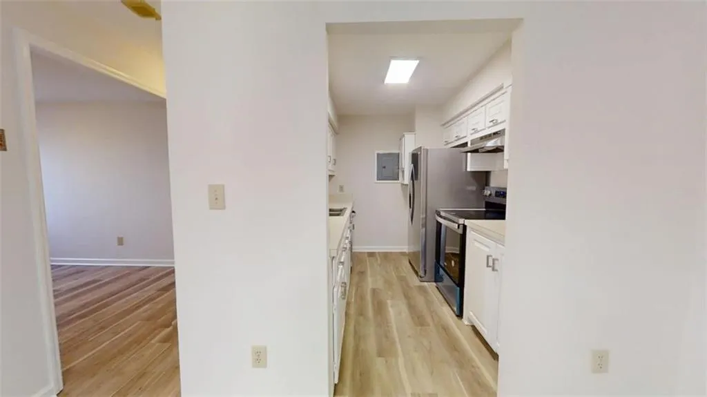 Kitchen featuring light wood finished floors, electric range, baseboards, white cabinets, and under cabinet range hood
