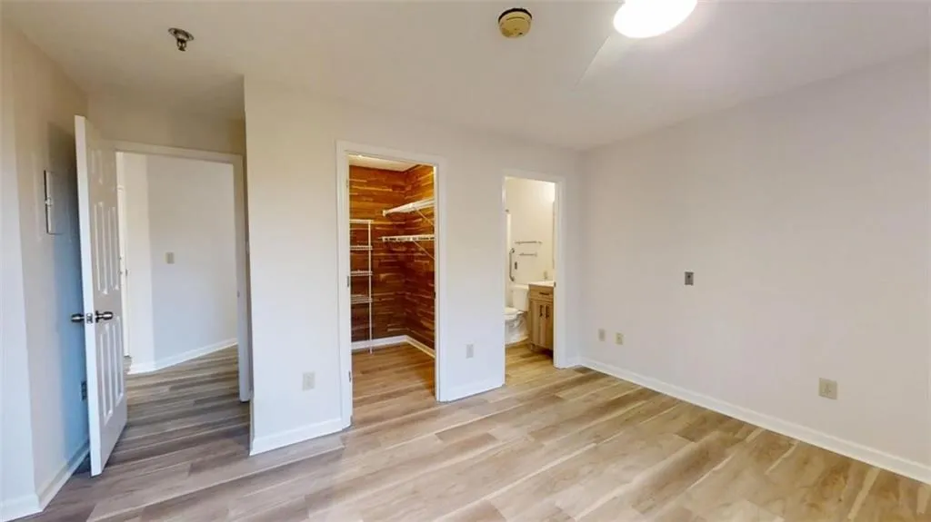 Unfurnished bedroom featuring light wood-style flooring, baseboards, a spacious closet, a closet, and ensuite bath
