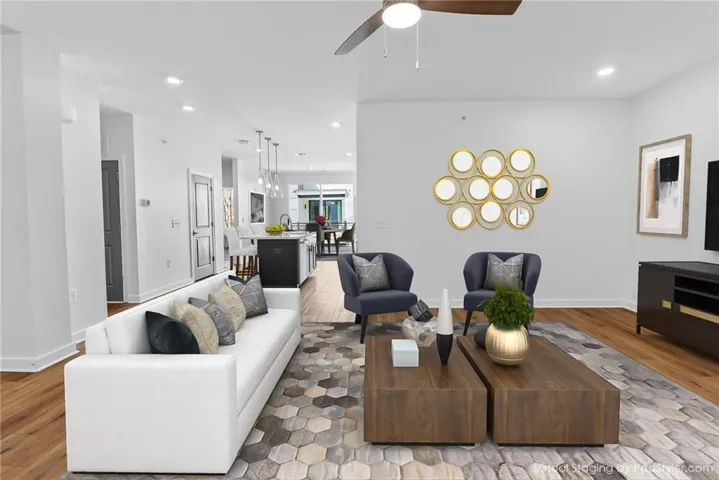 Open-concept living space featuring a white sectional sofa, wood-finish flooring throughout, with tall white walls
