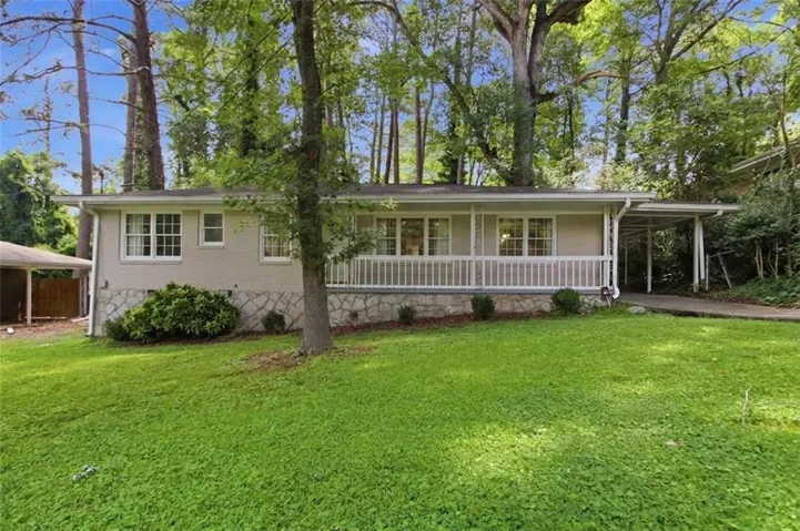 Ranch-style residence featuring a stone veneer foundation, expansive front lawn, and a full-width covered porch with white railing