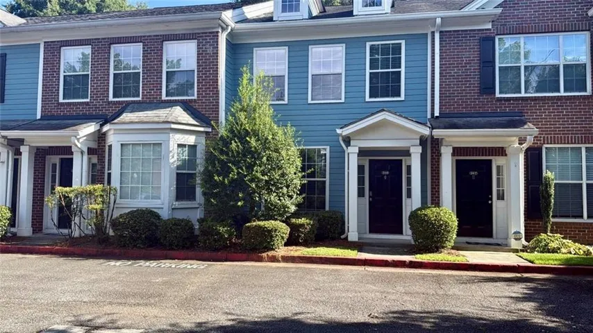Brick and siding townhome featuring multiple covered entry porticos with columned supports, black paneled front doors, and manicured foundation plantings