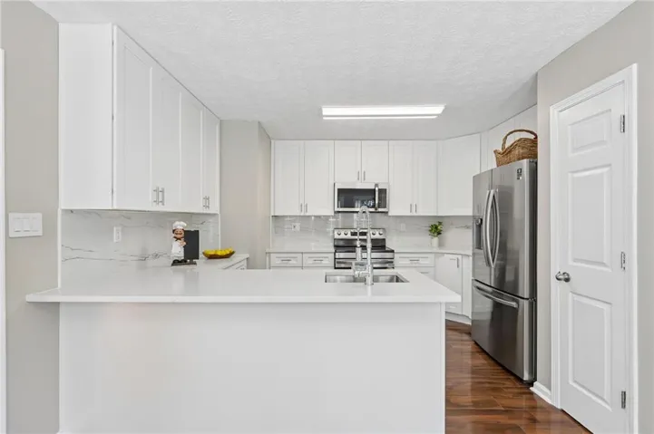 Kitchen featuring white cabinetry, stainless steel appliances, white countertops, a single basin sink, and wood-finish flooring