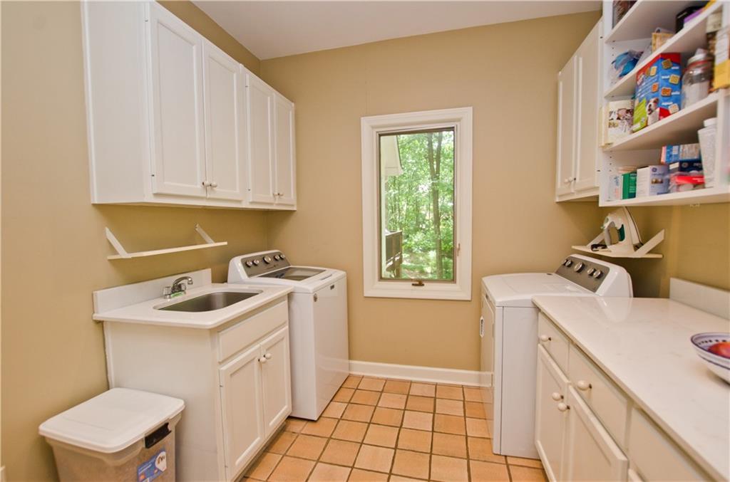 Large laundry room located off the kitchen with cabinets and shelves as well as a laundry sink