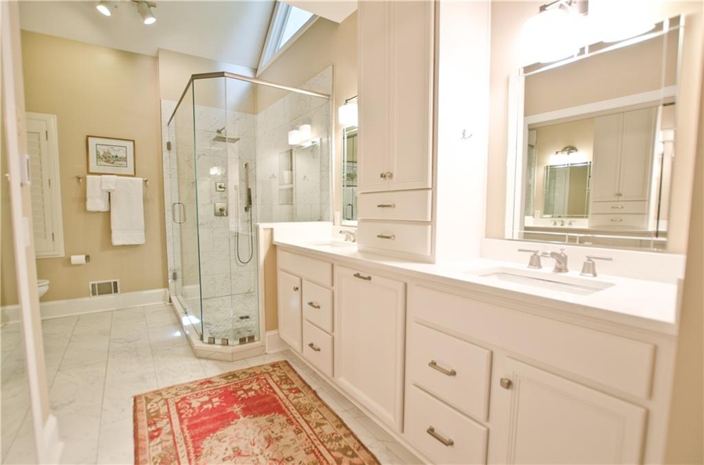The renovated primary bath features tile counters / walk-in glass shower / double vanities/