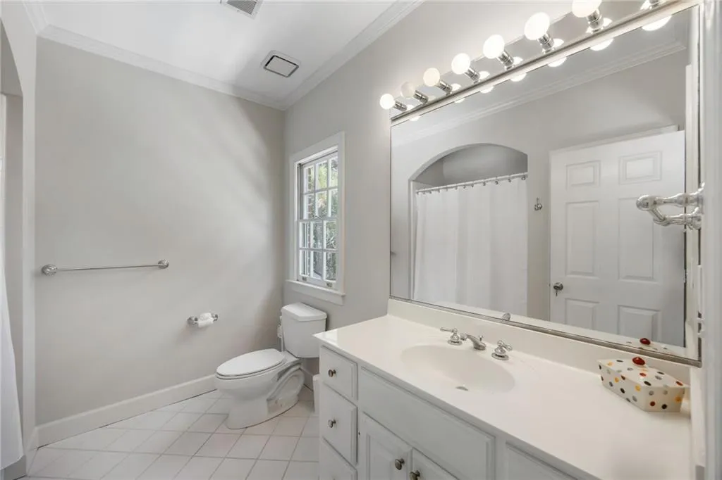 White tile flooring, single-pane window, single vanity with integrated sink, chrome faucet, and full-width mirror with overhead lighting