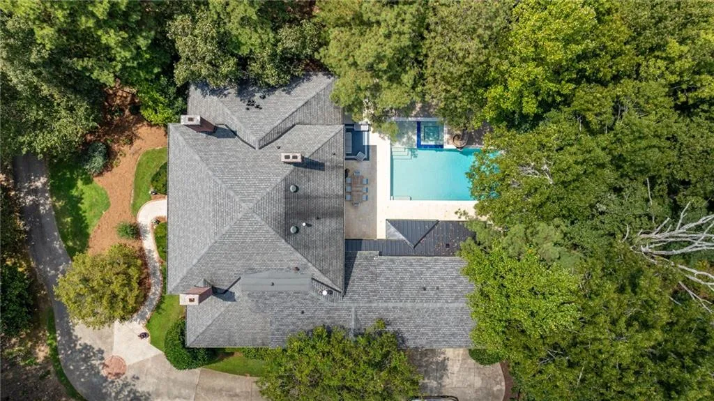 Asphalt shingle roofing, multiple chimneys, rectangular swimming pool, integrated spa, and extensive surrounding foliage