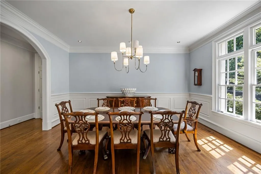 Wood-finish flooring, white paneled wainscoting, crown molding, and an arched doorway