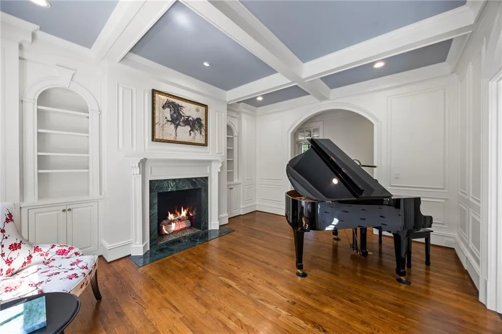 Coffered ceiling, polished wood-finish flooring, built-in shelving, fireplace with stone surround, and an arched entryway