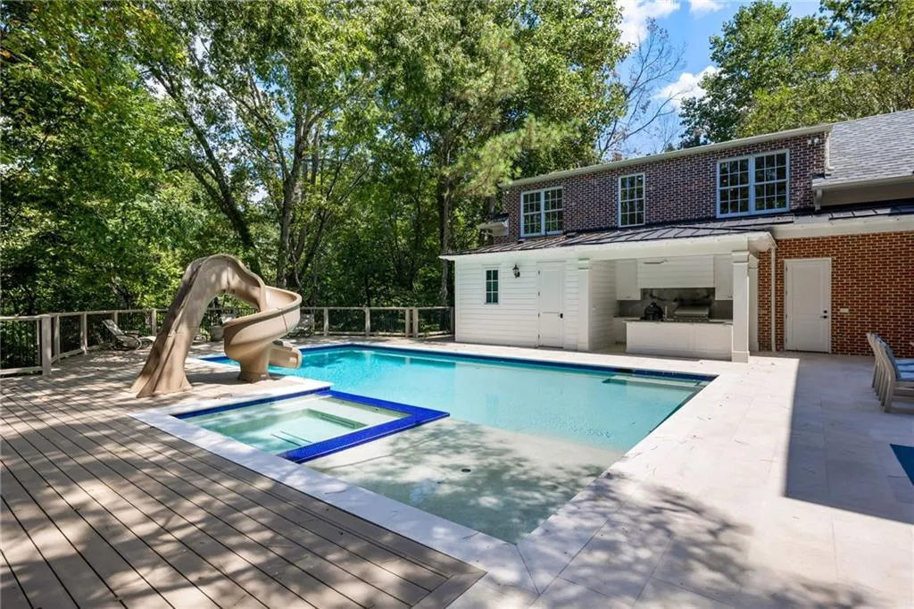 Pool with integrated spa, adjacent outdoor kitchen, and waterslide feature
