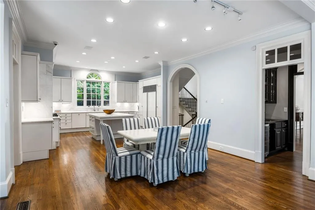 Hardwood flooring extending into a kitchen with white cabinetry and a central island