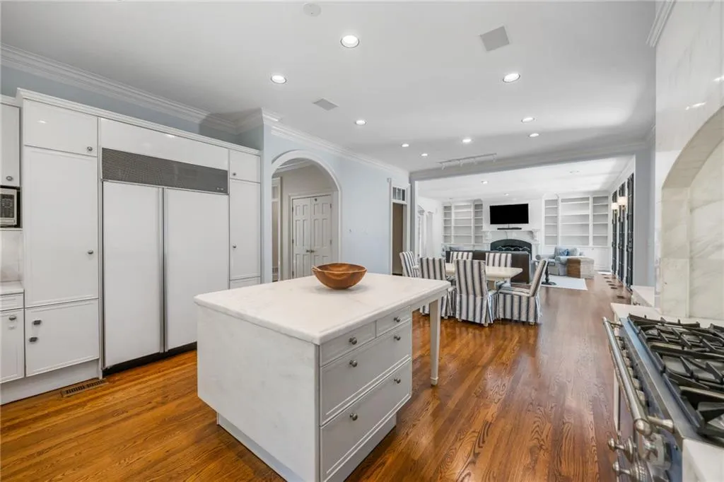 Kitchen featuring a center island with a light-toned countertop, built-in panel-front refrigeration, wood-finish flooring, recessed lighting, and a gas range