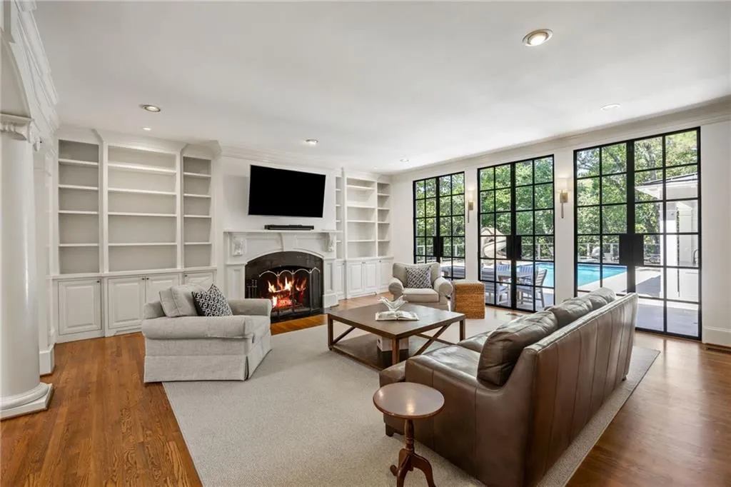 Hardwood flooring, recessed lighting, built-in shelving, fireplace with stone surround, and large grid-pattern windows