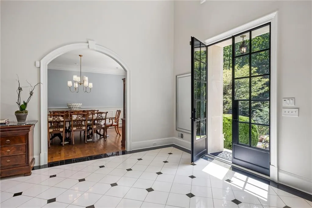 Gridded glass double doors, white and black checkerboard tile flooring, arched entryway, and wood-finish flooring
