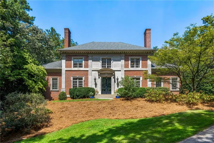 Brick and stone facade residence featuring a slate roof, prominent dual brick chimneys, and an ornamental front entrance with a portico
