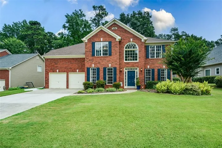 Brick facade residence featuring a prominent arched window, blue shutters, a two-car garage, and a concrete driveway
