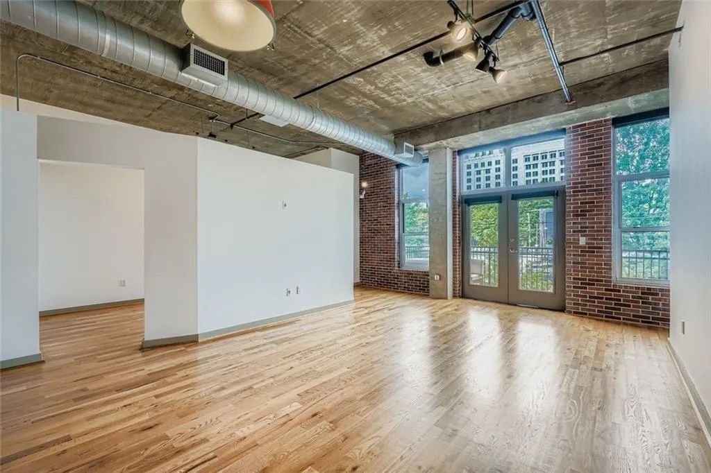 Unfurnished living room featuring brick wall, light wood-type flooring, and french doors