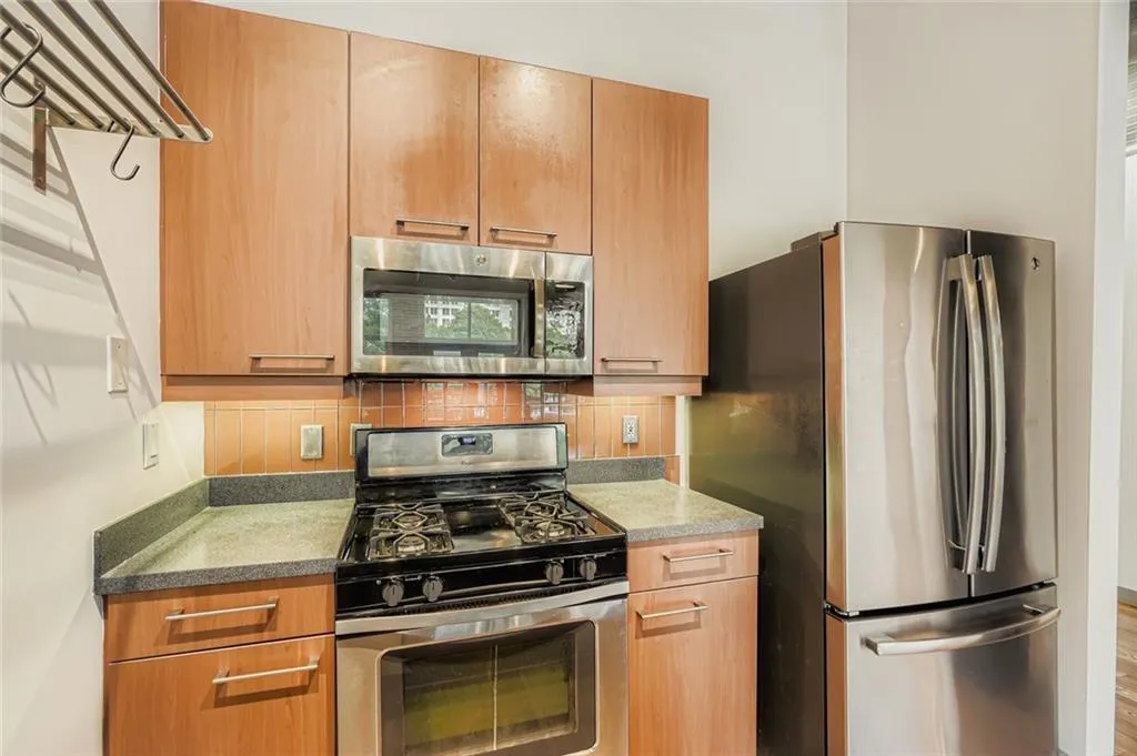 Kitchen with decorative backsplash, appliances with stainless steel finishes, brown cabinetry, and dark stone countertops