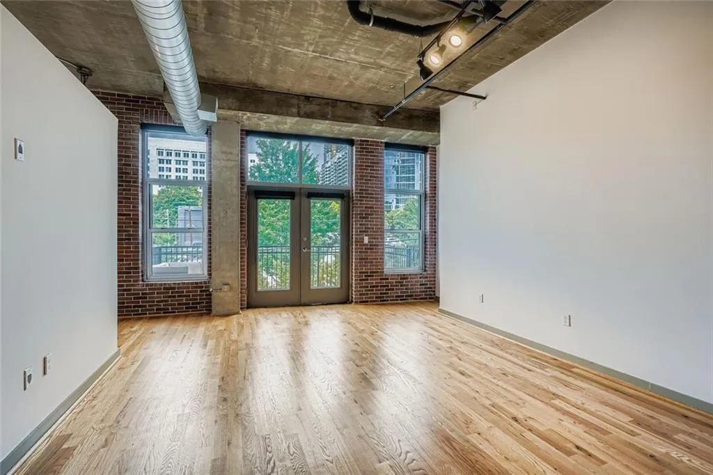 Empty room with plenty of natural light, brick wall, wood finished floors, and french doors