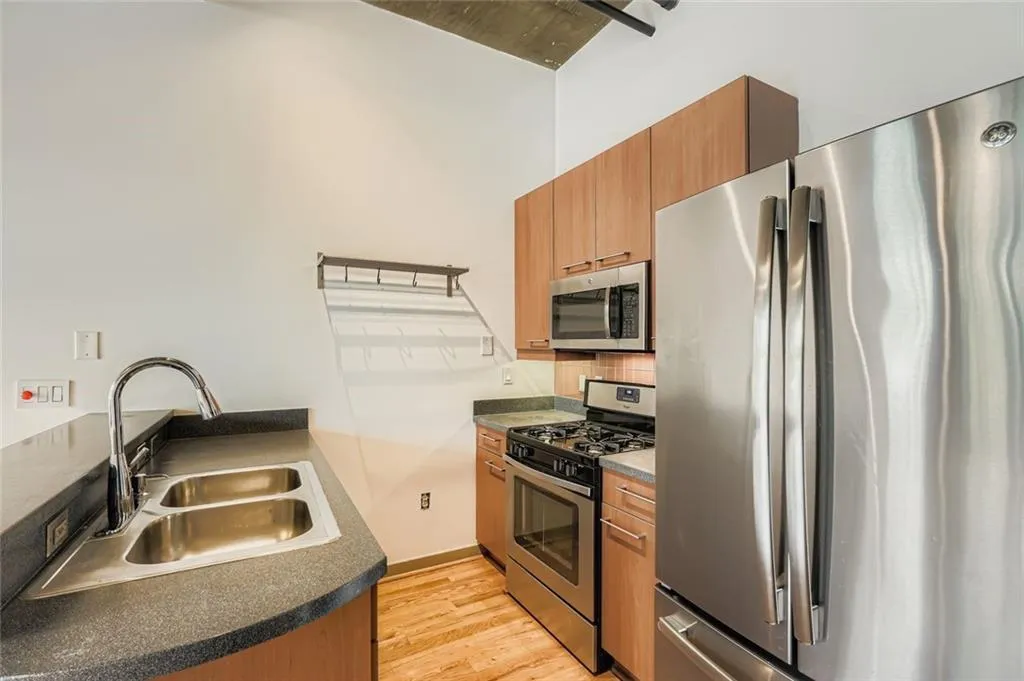 Kitchen featuring stainless steel appliances, brown cabinetry, light wood finished floors, dark countertops, and tasteful backsplash