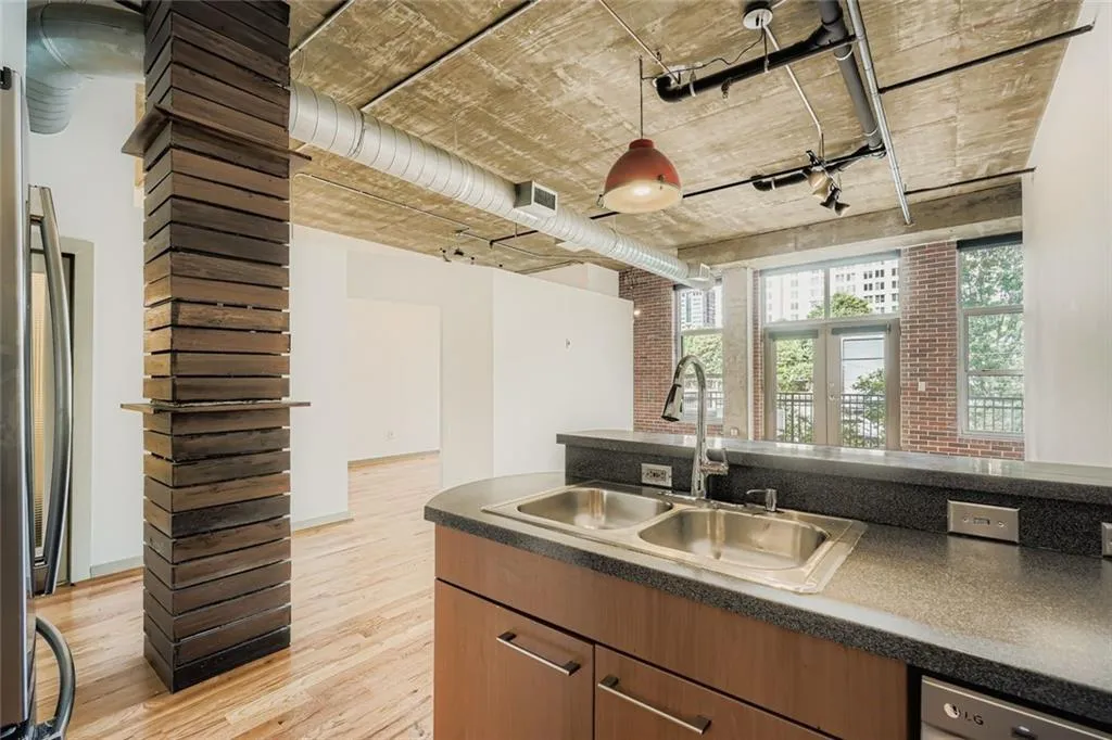 Kitchen featuring decorative light fixtures, light wood finished floors, appliances with stainless steel finishes, brown cabinetry, and brick wall