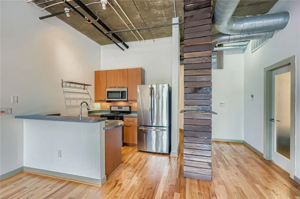 Kitchen with appliances with stainless steel finishes, a towering ceiling, brown cabinets, light wood-style flooring, and a peninsula