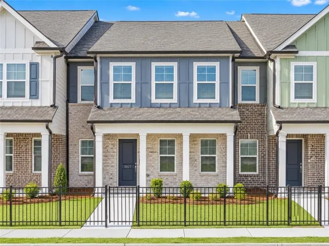 Modern townhome with a covered porch, brick facade, board and batten siding, and a fenced yard