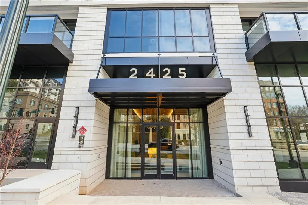 Modern building exterior featuring a prominent awning over the main entrance, large paneled windows, and glass-railed balconies