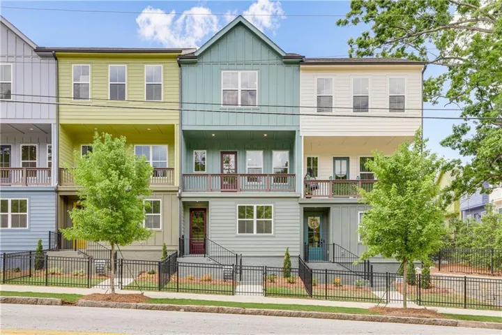 Multi-story townhome featuring board and batten siding, multiple balconies with wood railings, and a black metal fence