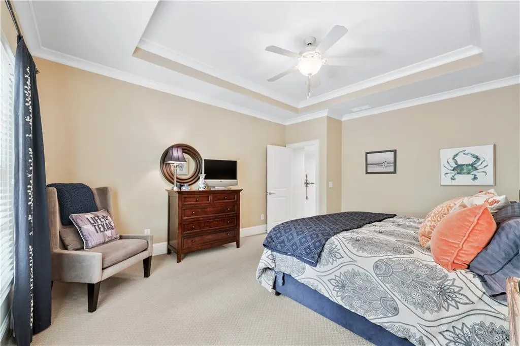 Bedroom featuring a tray ceiling, light colored carpet, crown molding, and a ceiling fan