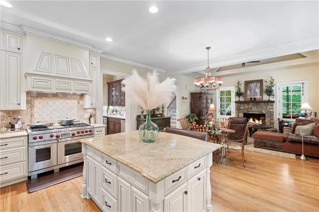 Kitchen featuring range with two ovens, light wood-type flooring, a chandelier, backsplash, and a stone fireplace