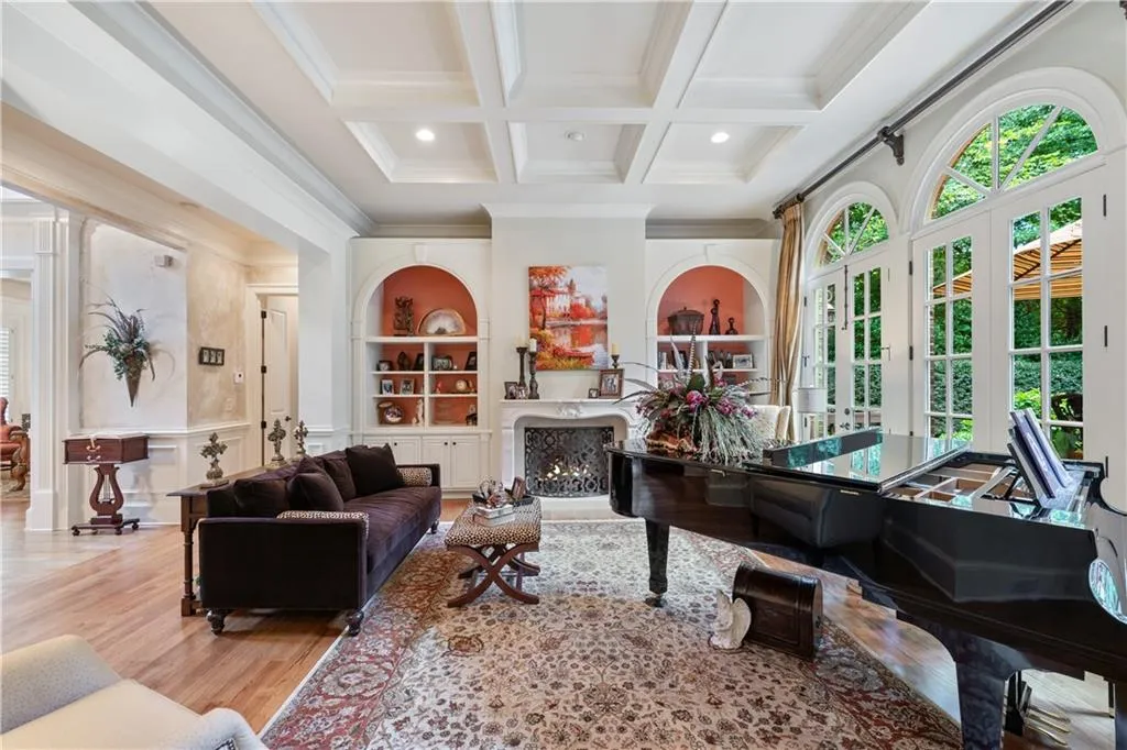 Living room with crown molding, a warm lit fireplace, coffered ceiling, wood finished floors, and beamed ceiling