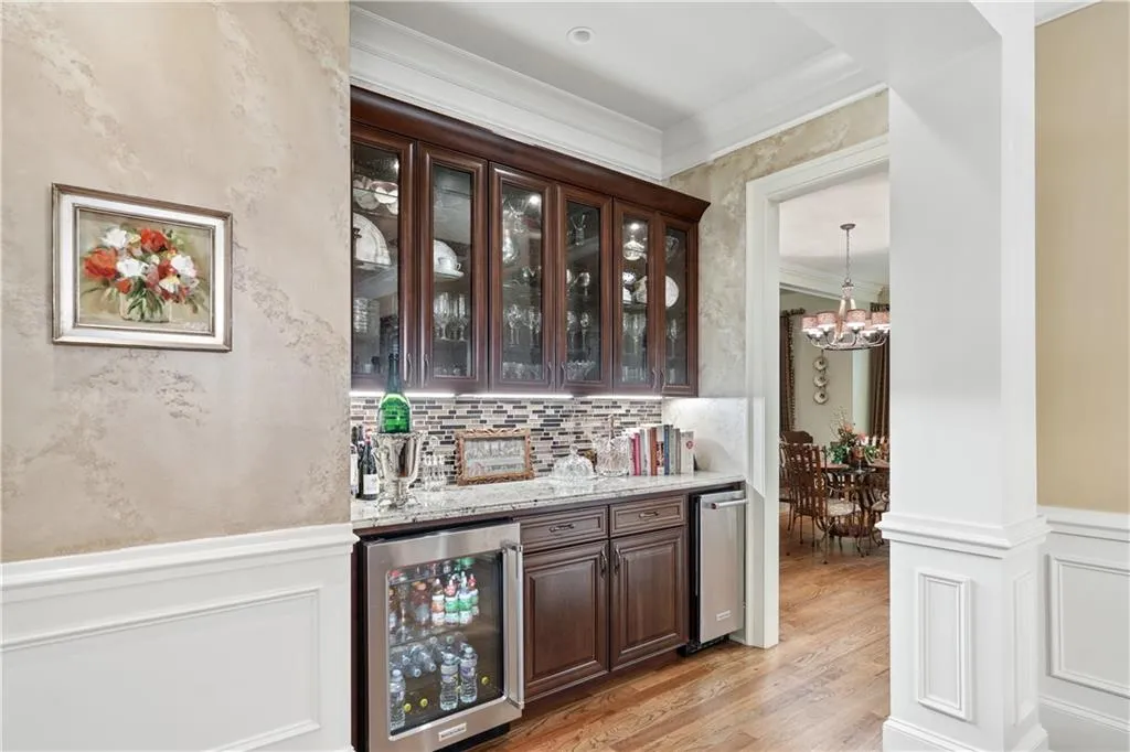 Indoor bar featuring wine cooler, a chandelier, light wood-style floors, ornamental molding, and wainscoting